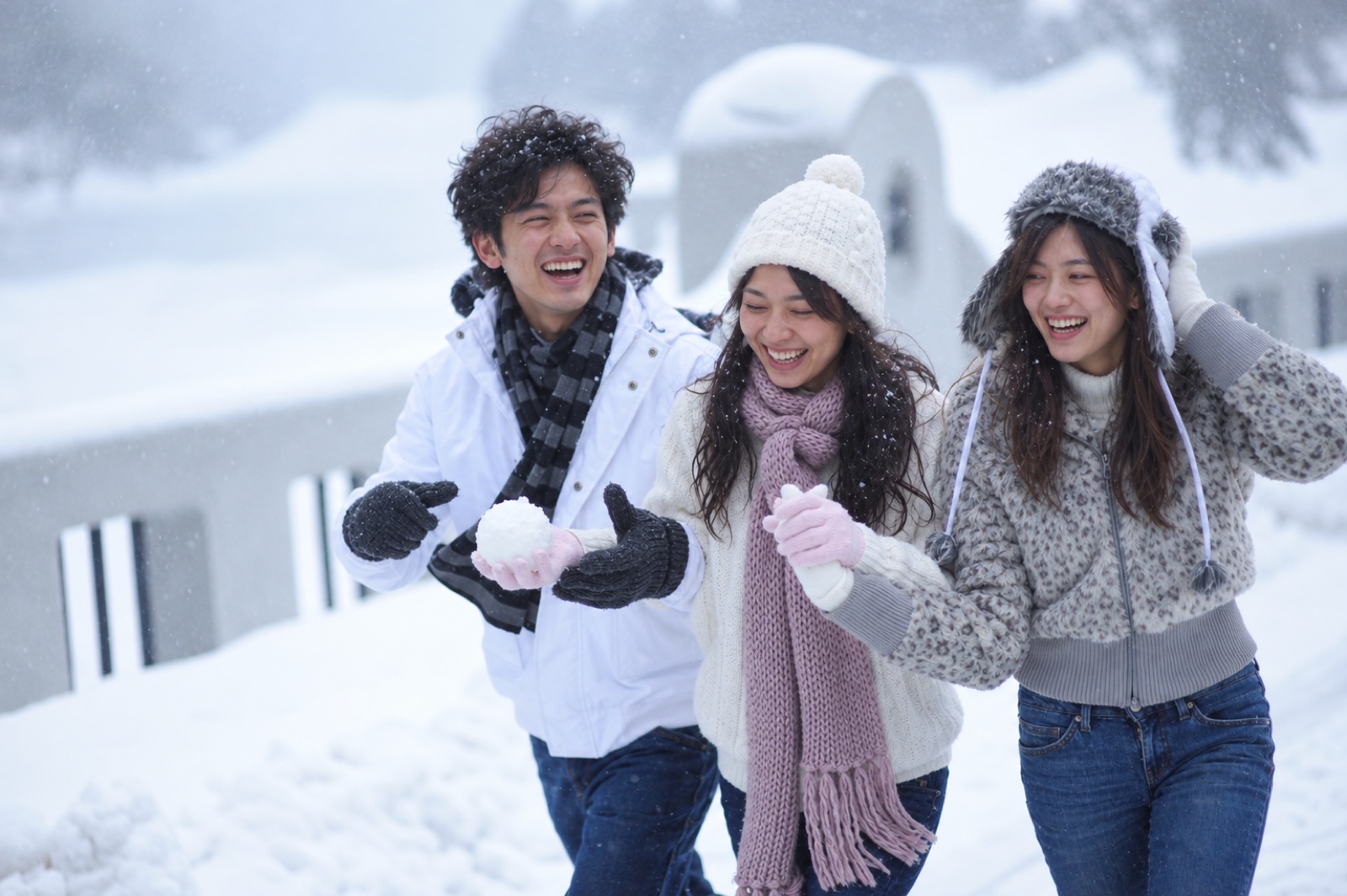 三位旅伴在落雪中捧著雪球，自然地笑著